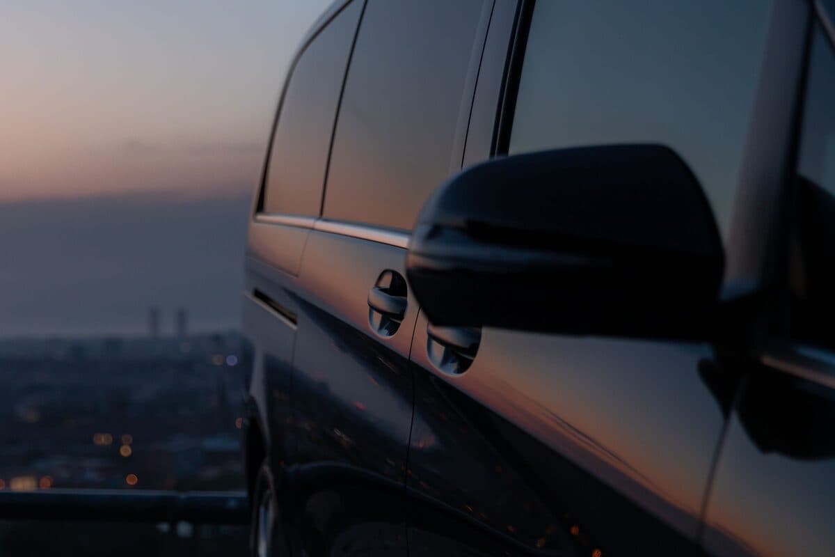 A dark chauffeur van at dusk, city lights below