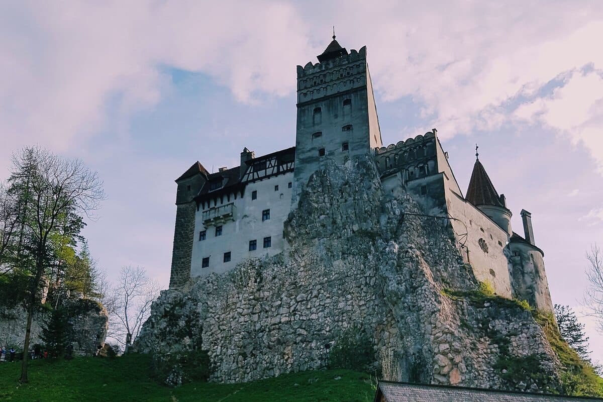 Bran Castle on its rock, with a traditional wooden house in the foreground