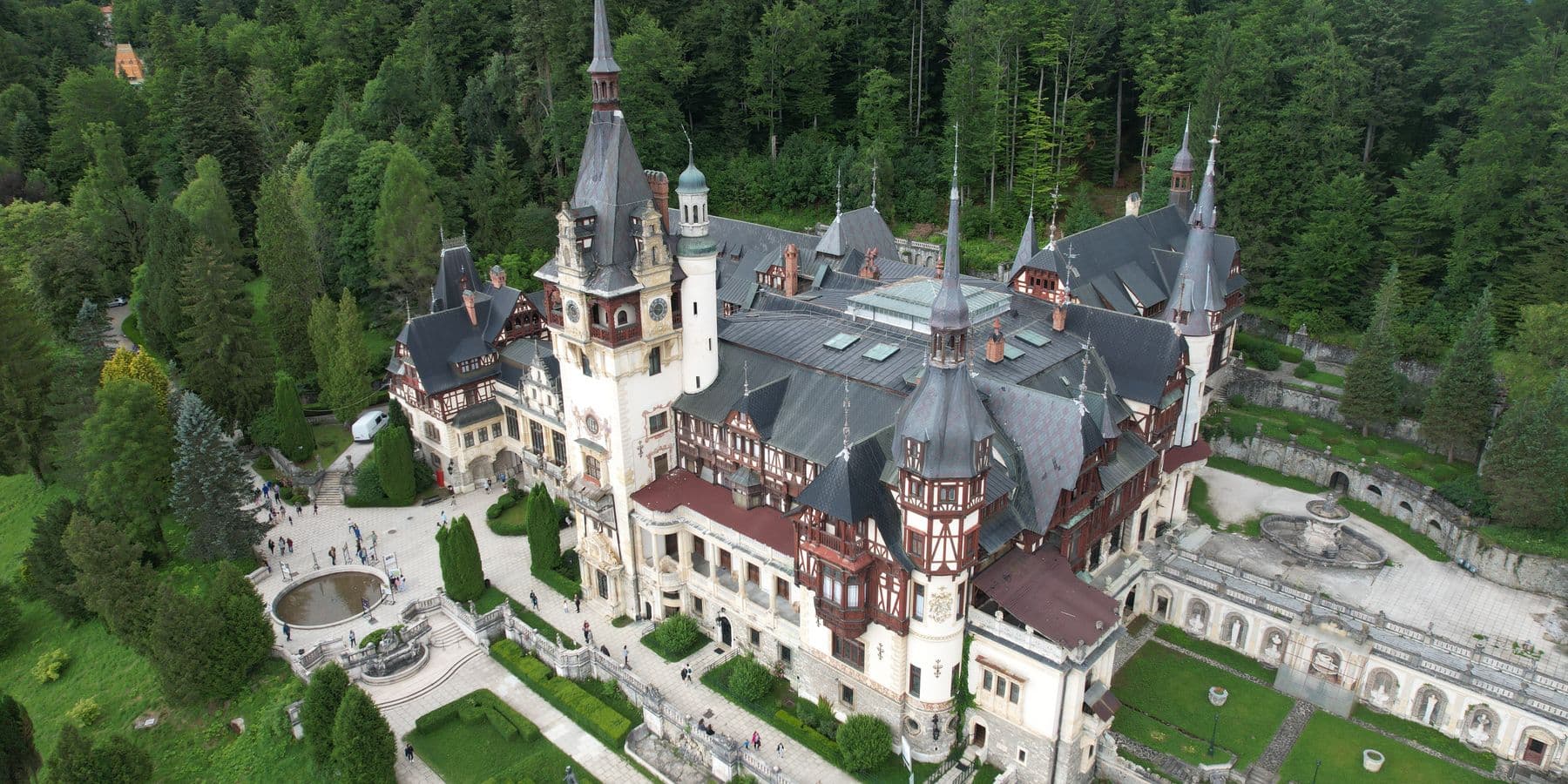 Peleș Castle in Sinaia seen from above, ringed by Carpathian forest